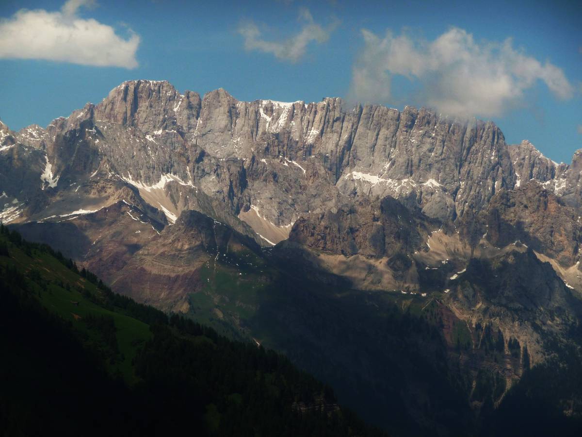 The south wall of Marmolada, also known as the “silver wall”, with Monte La Banca, Monte Fop and Cime dell'Auta in the foreground from left to right. Marmolada, the Queen of the Dolomites, differs from the rest of the Dolomites in its limestone composition. The lack of dolomitisation of the Marmolada platform as well as the adjacent Costabella-Cime dell'Auta, can be put down to the absence of contact with sea water, as Marmolada was submerged in its entirety in watertight volcanic rocks throughout the Late Ladinian.   Marmolada Limestone (now Schlern Formation) has weathered with time; the massive areas alternate with vertical fractures that create jagged peaks at the top. The thus created landscape is similar in some ways to the granite of Val Masino-Bregaglia and on Mont Blanc. 